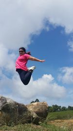 Woman jumping over land against blue sky