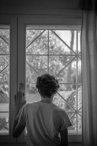 Rear view of man looking through window at home