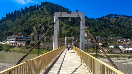 People on footbridge by mountain against sky