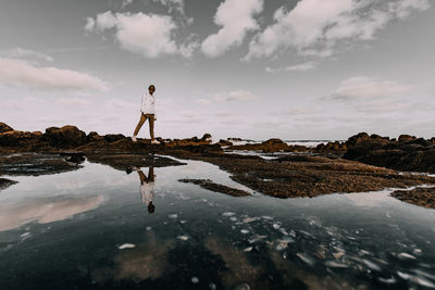 Man standing on rock at beach against sky