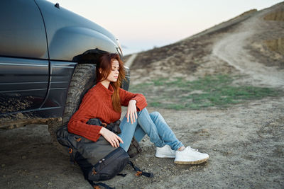 Young woman sitting on land against the sky