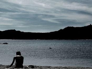 Rear view of silhouette woman standing by sea against sky