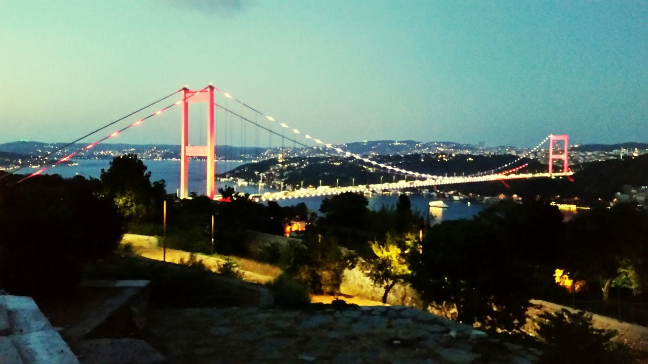 bridge - man made structure, connection, built structure, suspension bridge, illuminated, architecture, engineering, transportation, sky, travel destinations, outdoors, night, city, bridge, no people, tree, water, mountain