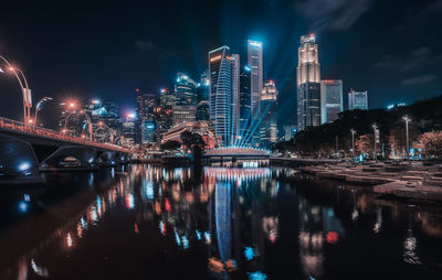 Illuminated bridge over river by buildings against sky at night