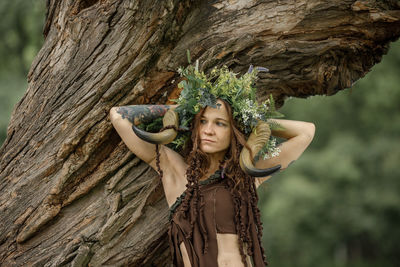 Portrait of woman standing against tree trunk