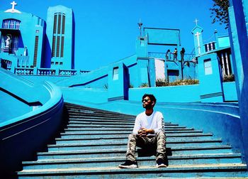 Man sitting on staircase against blue sky