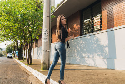 Portrait of young woman standing on footpath against built structure in city