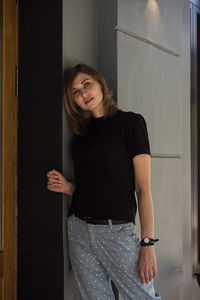 Portrait of young woman standing against door