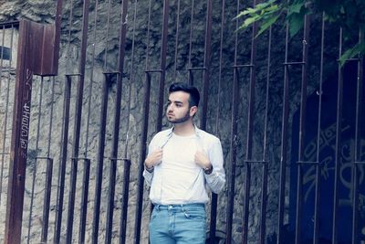 Young man looking away while standing against wall