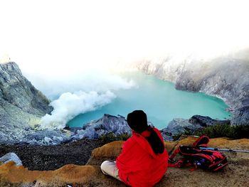 Rear view of man sitting on rock against sky