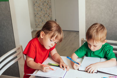 Children sit at the table and write in notebooks. homeschooling concept, learning online
