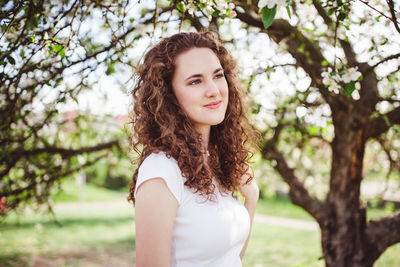 Happy curly hair young woman in a white t-shirt under the blooming apple tree. smiling.