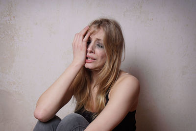 Upset young woman crying against wall