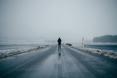 Person standing on empty road against sky during foggy weather