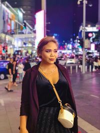 Portrait of young woman standing on street at night