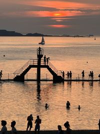 Silhouette people on sea against sky during sunset