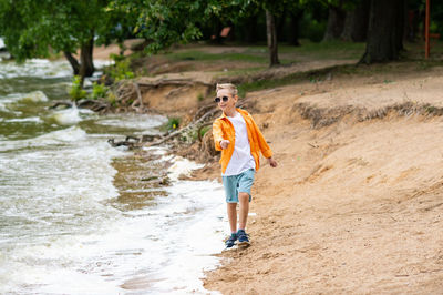 A boy in an orange shirt on the seashore. a child in sunglasses person