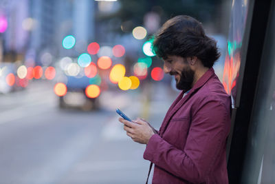 Young man with smartphone at night time with city view  in the background. mobile, technology, urban 