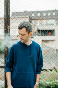 Mid adult man looking through chainlink fence