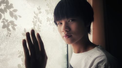 Portrait of boy looking through window at home