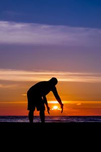 Silhouette man bending at beach against sky during sunset
