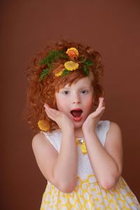 Portrait of girl with herb and vegetables in her hair against brown background