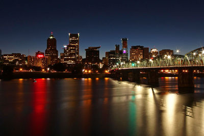 Illuminated buildings by river against sky at night