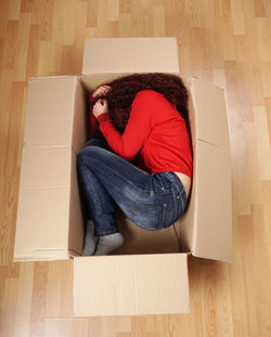 High angle view of woman lying in cardboard box at home