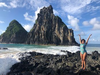 Woman standing on rock by sea against sky