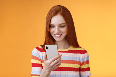 Portrait of smiling young woman using smart phone against orange background