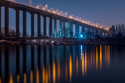 Illuminated bridge over river against sky at night