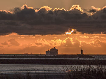 Silhouette of lighthouse against cloudy sky during sunset