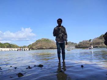 Man standing in sea against blue sky