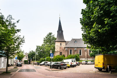 Road amidst trees and buildings against sky