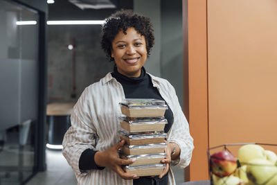 Happy young woman with take away food boxes standing in office