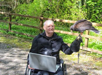 Portrait of man with laptop holding falcon while sitting in park