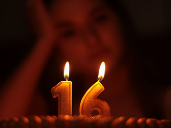 Close-up of teenage girl with illuminated candles on birthday cake in darkroom