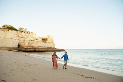 Rear view of woman walking at beach against clear sky