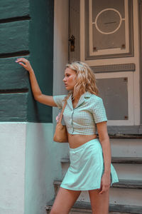 Woman looking away while standing against wall