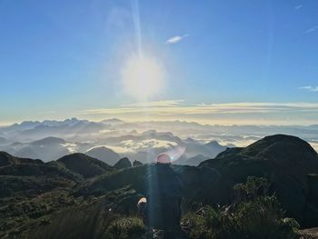 Rear view of man sitting on mountain against landscape during sunny day