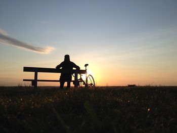Silhouette man sitting on field against sky during sunset