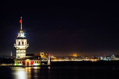 Illuminated buildings by river against sky at night