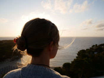 Rear view of woman looking at sea against sky during sunset