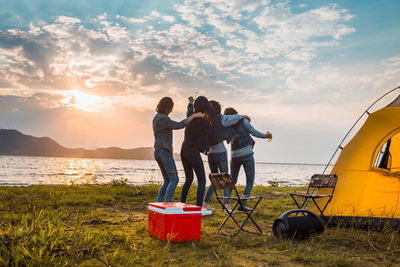 People standing on beach by sea against sky during sunset