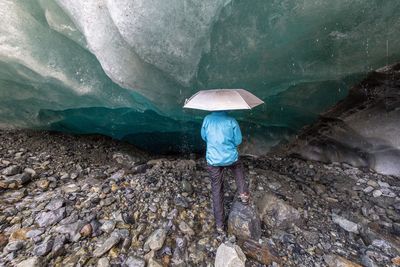 Rear view of person with umbrella standing by glacier