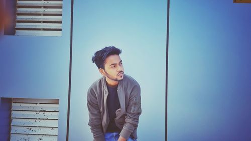 Thoughtful young man sitting against blue wall