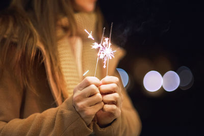 Midsection of person holding sparkler against illuminated lights at night