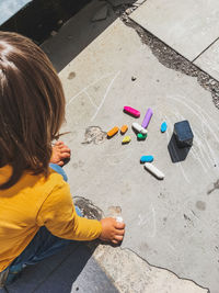 Toddler in jeans draws with crayons on the asphalt in sunny day. kid's hands are covered with stain. 