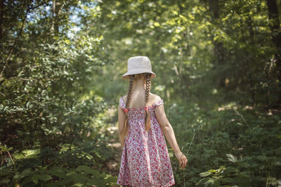 Rear view of cute girl wearing hat standing against trees