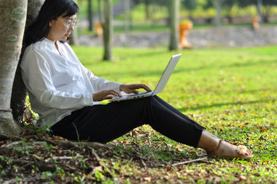 Woman using mobile phone while sitting on field